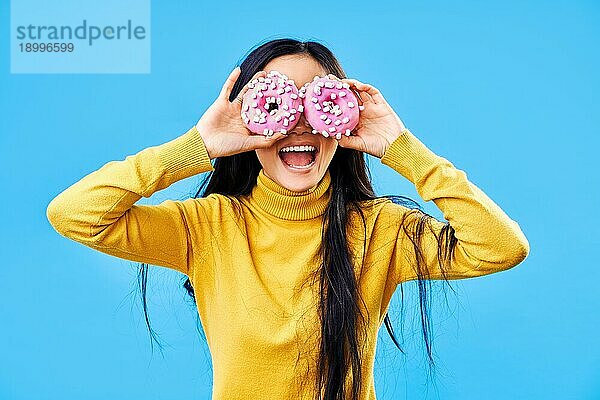 Attraktive Frau hat Spaß mit Donuts. Mädchen zeigt Donuts vor ihren Augen auf blauem Hintergrund. Leckeres Essen  Diätkonzept