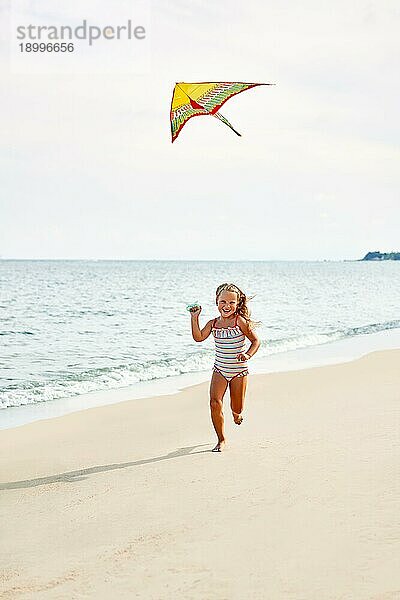 Glückliches Kind Mädchen mit einem Drachen läuft auf tropischen Strand. sorglose Kindheit Konzept
