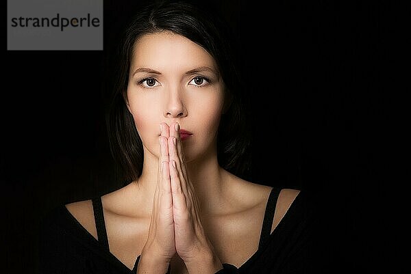 Dunkles  stimmungsvolles Porträt einer spirituellen jungen Frau  die mit gefalteten Händen und einem absichtlichen Blick betet
