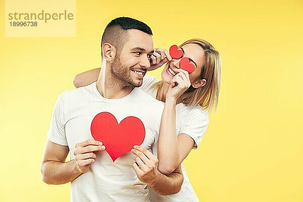 Glückliches Paar in der Liebe haben Spaß mit Papier Herzen auf gelbem Hintergrund. Beziehung und romantisches Konzept