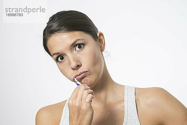 Attraktive Frau bei der Zahnpflege  die sich mit Zahnbürste und Zahnpasta die Zähne putzt  um Karies vorzubeugen  vor weißem Hintergrund