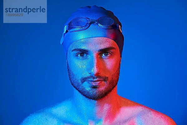 Close up Porträt von gut aussehend Schwimmer mit Schwimmbrille in rot rosa Neonlicht über blauem Hintergrund. Sport  Mode  männliche Schönheit