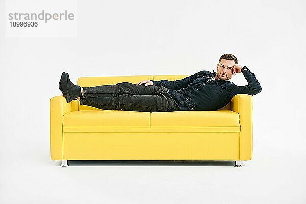 Junger Mann entspannt allein auf gelbem Sofa zu Hause. Ruhe Konzept