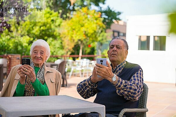Zwei sehr glückliche ältere Menschen im Garten eines Pflegeheims  die auf das Telefon schauen  Technologien im Alter