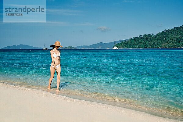 Schöne junge Frau in weißem Bikini und Strohhut zu Fuß auf tropischen Strand im Paradies Insel. Entspannen  Urlaub  Reisen Konzept