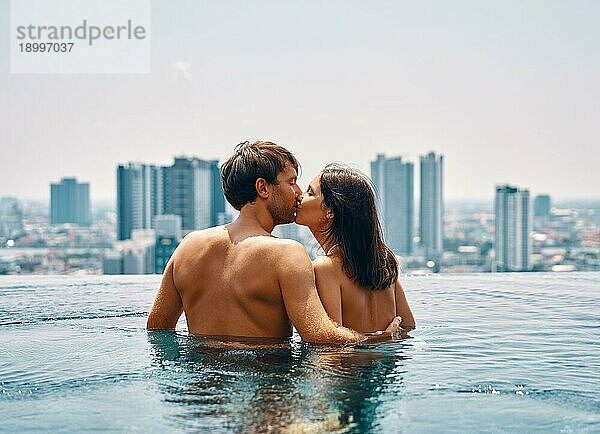 Junges glückliches Paar küsst sich im Schwimmbad im Sommerurlaub