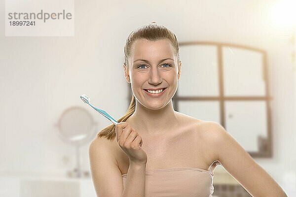 Lächelnde  gesunde Frau mit nackten Schultern und einem freundlichen Lächeln  die eine Zahnbürste in der Hand hält Konzept der Zahnmedizin  Mundhygiene und Kariesprävention