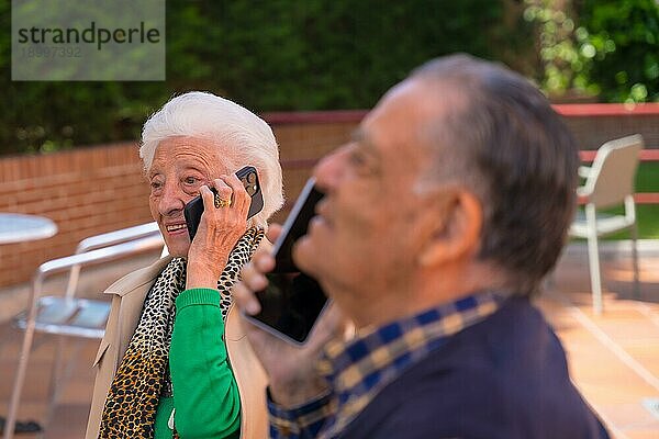 Zwei ältere Menschen im Garten eines Altenheims  die miteinander telefonieren  Technologien für ältere Menschen