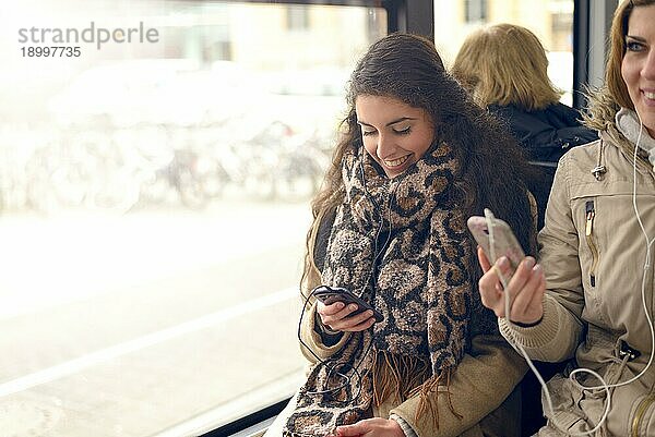 Glückliche brünette Frau  die eine Nachricht auf ihrem Handy liest  während sie in einem Bus sitzt  öffentliche Verkehrsmittel und Technologiekonzept