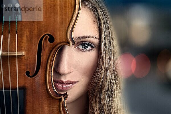 Close up Pretty Young Woman Peeking Behind Violin Instrument vor Lichter in den Abend oder die Nacht