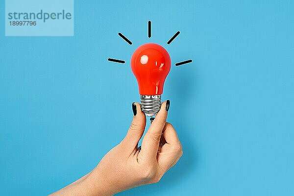 Weibliche Hand hält rote Glühbirne auf blauem Hintergrund. Kreative Idee  Innovation  Brainstorming Konzept