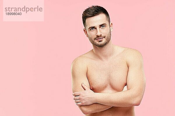 Porträt eines gutaussehenden  selbstbewussten  muskulösen Mannes mit verschränkten Armen und nacktem Oberkörper  der in die Kamera schaut  auf rosa Hintergrund. Leerzeichen kopieren