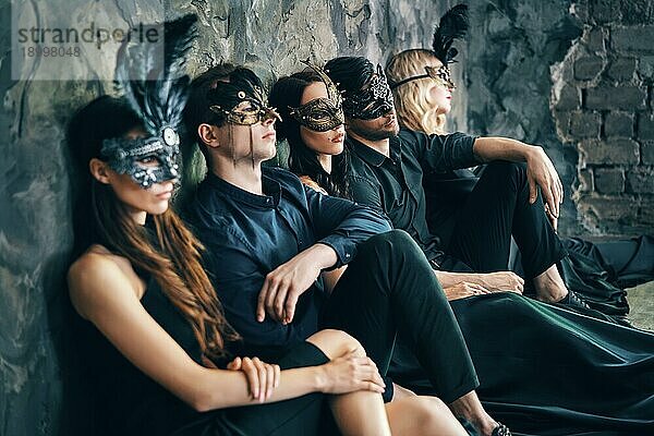 Gruppe von Freunden in Maskerade Karneval Maske sitzen auf dem Boden entspannen nach der Party. Schöne Frauen und Männer tragen venezianische Maske. Mode  Freunde Konzept