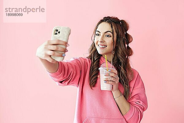 Junge trendige Frau macht Selfie Porträt hält Milchshake auf rosa Hintergrund. kreatives Konzept