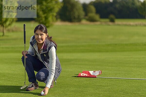 Attraktive Golferin  die einen Golfball vom Loch aufhebt  nachdem sie ein gutes Ergebnis gespielt hat  und in die Kamera lächelt