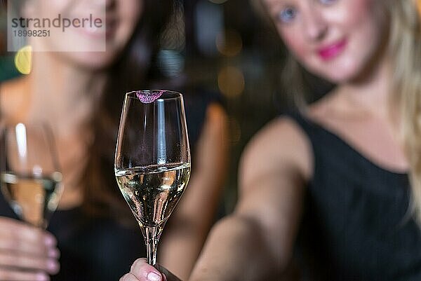 Fröhlich lächelnde Frauen  die in einem Restaurant oder Nachtclub mit Champagner feiern  mit Fokus auf das elegante Glas Champagner im Vordergrund