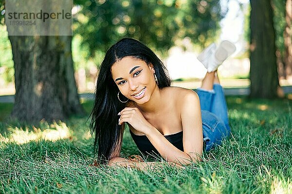 Hübsche lächelnde afroamerikanische Frau entspannt im Park auf grünem Gras liegend. Ruhe  weibliche Schönheit Konzept
