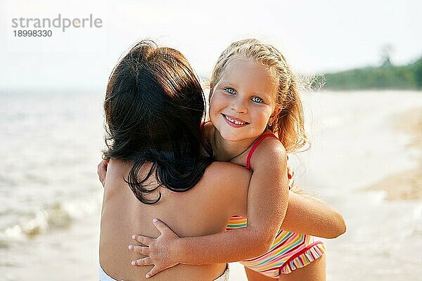 Junge Frau und ihre hübsche kleine Tochter sind umarmt und lächelnd auf dem tropischen Strand. Sommerurlaub  glückliche Familie  Liebe Konzept
