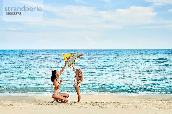 Mutter und Tochter haben Spaß beim Fliegen eines Drachens am tropischen Strand. Familienurlaub  Strand Spaß Konzept