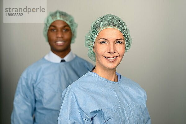 selbstbewusste männliche und weibliche medizinische Fachkräfte  die in die Kamera lächeln und blaue Kittel und Sterilitätskappen tragen