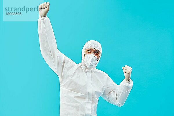 Glücklicher Arzt in PSA Anzug feiert seinen Erfolg mit Siegergeste und Hände hoch auf blauem Hintergrund. Sieg  Triumph und Emotionen Konzept
