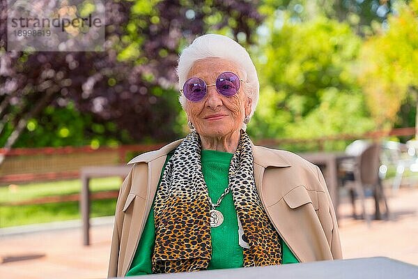 Eine ältere Frau im Garten eines Pflegeheims oder Seniorenheims bei einem Sommerfest mit Sonnenbrille