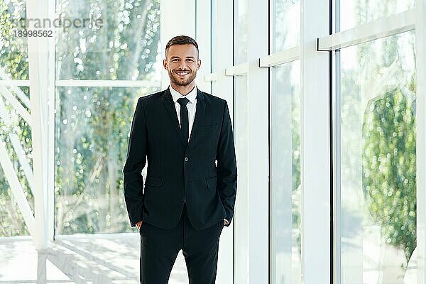 Selbstbewußt lächelnder Geschäftsmann in elegantem Anzug  der in einem modernen  kreativen Büro posiert. Menschen im Geschäft