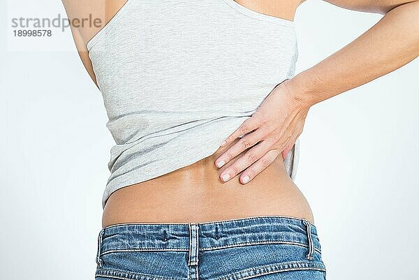 Rückansicht einer Frau mit Schmerzen im unteren Rücken  die sich mit den Händen an Rücken und Wirbelsäule festhält  um den Schmerz in den Muskeln oder in den Wirbeln und Bandscheiben zu lindern  der durch Stress  Verletzungen oder Krankheiten verursacht wird
