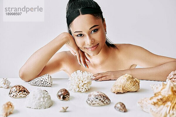 Lächelnde hübsche Afro Frau mit verschiedenen Muscheln auf weißem Hintergrund. Schönheit weibliches Porträt