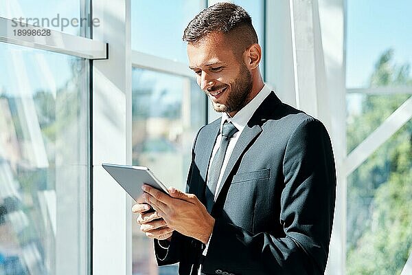 Junger lächelnder Geschäftsmann arbeitet an einem Tablet in einem modernen kreativen Büro. Business Technologie