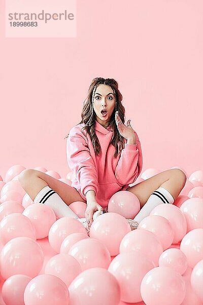 Junge trendy überrascht Frau mit rosa Luftballons auf rosa Pastell Hintergrund. kreatives Konzept. Menschen Emotionen