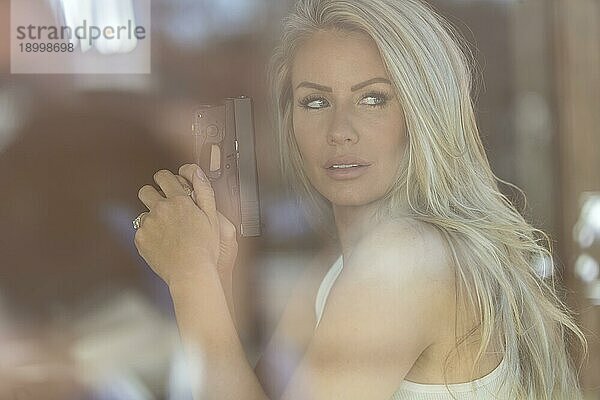 Ein schönes blondes Modell hält eine Pistole zum Schutz an einem sonnigen Tag