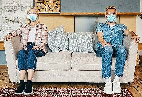 Mann und Frau mit Gesichtsmaske sitzen zu Hause auf dem Sofa. Soziale Distanzierung  Konzept des Coronavirus