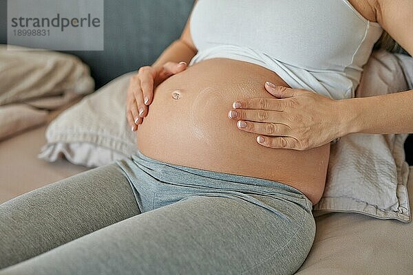 Junge schwangere Frau  die ihren Bauch mit Feuchtigkeitscreme einreibt  um ihre Haut mit Feuchtigkeit zu versorgen und die Gefahr von Schwangerschaftsstreifen nach der Geburt zu verringern