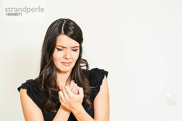 Attraktive junge weinerliche verzweifelte Frau mit geschlossenen Augen  die ihre Hände mit einem Ring in der Hand vor einem weißen Hintergrund verzweifelt ringt