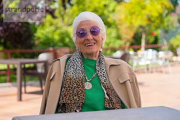 Eine ältere Frau lächelt im Garten eines Pflegeheims oder Seniorenheims bei einem Sommerfest und trägt eine Sonnenbrille