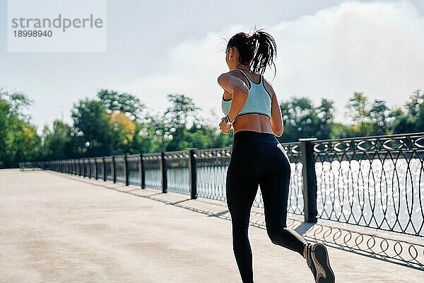 Rückenansicht einer fitten Frau beim Laufen im Freien am Fluss. Schöne Frau in Sportkleidung joggt im Freien. Dynamische Bewegung