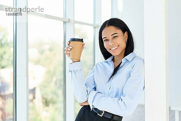 Glückliche schwarze Geschäftsfrau mit einer Tasse Kaffee in der Hand während der Pause in einem modernen Büro mit Kopierraum. Entspannen  Erfolg Konzept