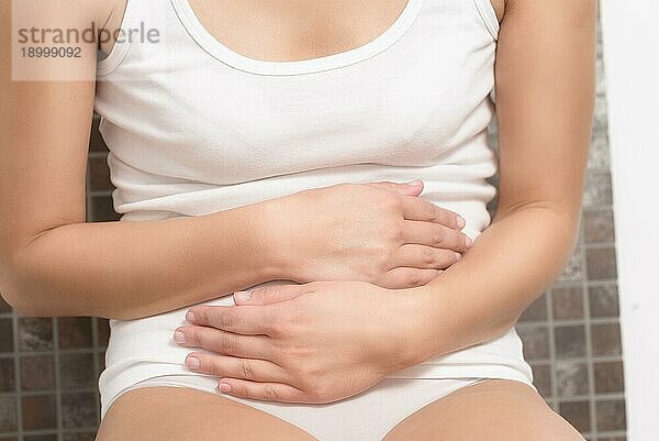 Frau mit monatlichen Menstruationsbeschwerden  die sich mit den Händen an den Bauch klammert  da sie durch die anhaltenden Krämpfe gestresst ist  Torsoansicht ihrer Hände und ihres Bauches  vor weißem Hintergrund