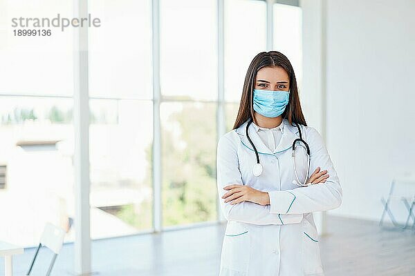 Ärztin mit medizinischer Maske und verschränkten Armen im Krankenhaushintergrund. Raum kopieren. Medizin  Beruf und Gesundheitswesen Konzept