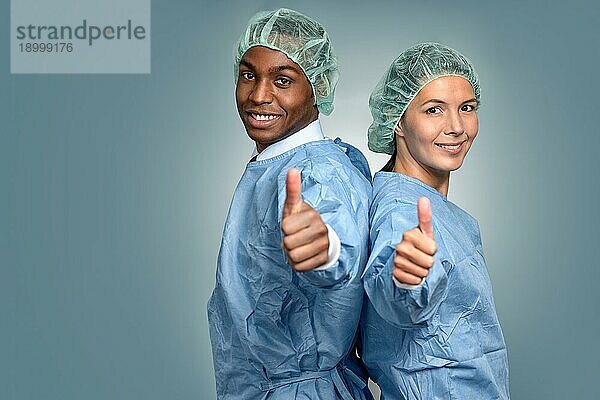 Hübscher junger afrikanischer Arzt oder Krankenpfleger in Kittel und Sterilitätskappe  der direkt in die Kamera schaut  vor grauem Hintergrund  Kopf Schulter Porträt