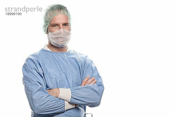 Freundlicher Krankenpfleger oder Arzt in OP Kleidung  der einen OP Kittel  eine Maske  eine Schutzbrille und eine Kappe trägt und direkt in die Kamera schaut  Kopf und Schultern vor weißem Hintergrund