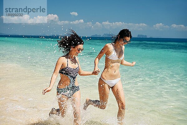 Zwei junge Frauen  die Spaß haben  lachen und laufen auf dem tropischen Strand während des Sommerurlaubs. Freiheit  Reiseziel  entspannen Konzept