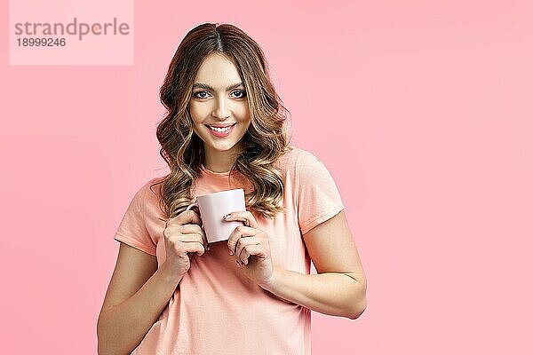 Lächelnde hübsche Frau genießt Tasse Aroma Kaffee auf rosa Hintergrund. Entspannen und ausruhen Konzept