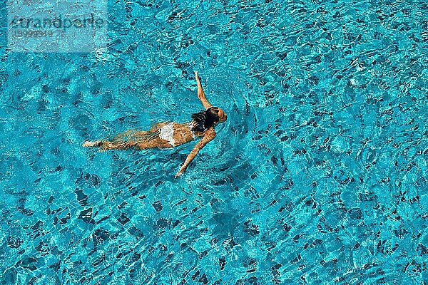 Blick von oben auf junge Frau schwimmen in sauberen türkisfarbenen Wasser im Infinity Pool. Entspannen  Urlaub  Sport Konzept