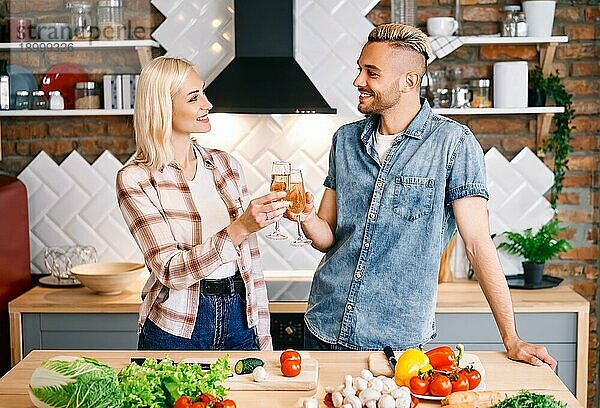 Junges glückliches Paar trinkt Champagner und genießt die Gesellschaft von einander in der Küche zu Hause. Beziehung  Feier Konzept