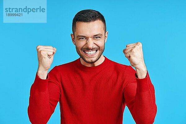 Glücklicher Mann feiert seinen Erfolg mit Gewinner Geste auf blauem Hintergrund. Sieg  Triumph und Emotionen Konzept