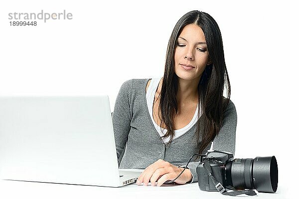 Junge  attraktive Frau  die eine DSLR Kamera an einen Laptopcomputer anschließt  um Fotos und Videos zu übertragen  vor weißem Hintergrund