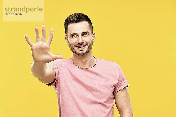 Porträt eines lächelnden Mannes mit zum Gruß erhobener Hand auf gelbem Hintergrund. High five  hallo Konzept
