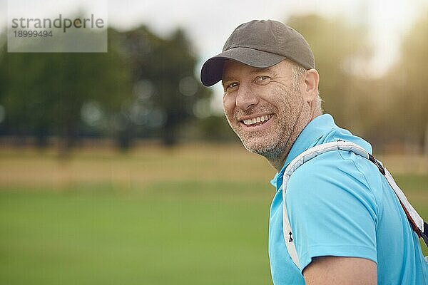 Lächelnder  freundlicher Golfer mittleren Alters  der sich umdreht  um über seine Schulter in die Kamera auf dem Fairway oder dem Grün zu schauen